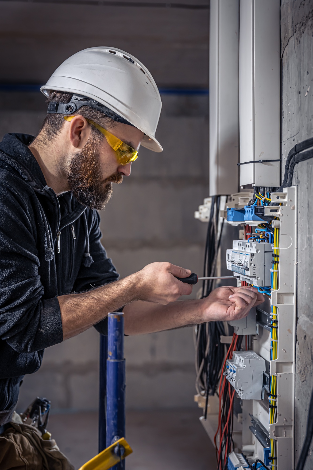 A male electrician works in a switchboard with an electrical connecting cable.