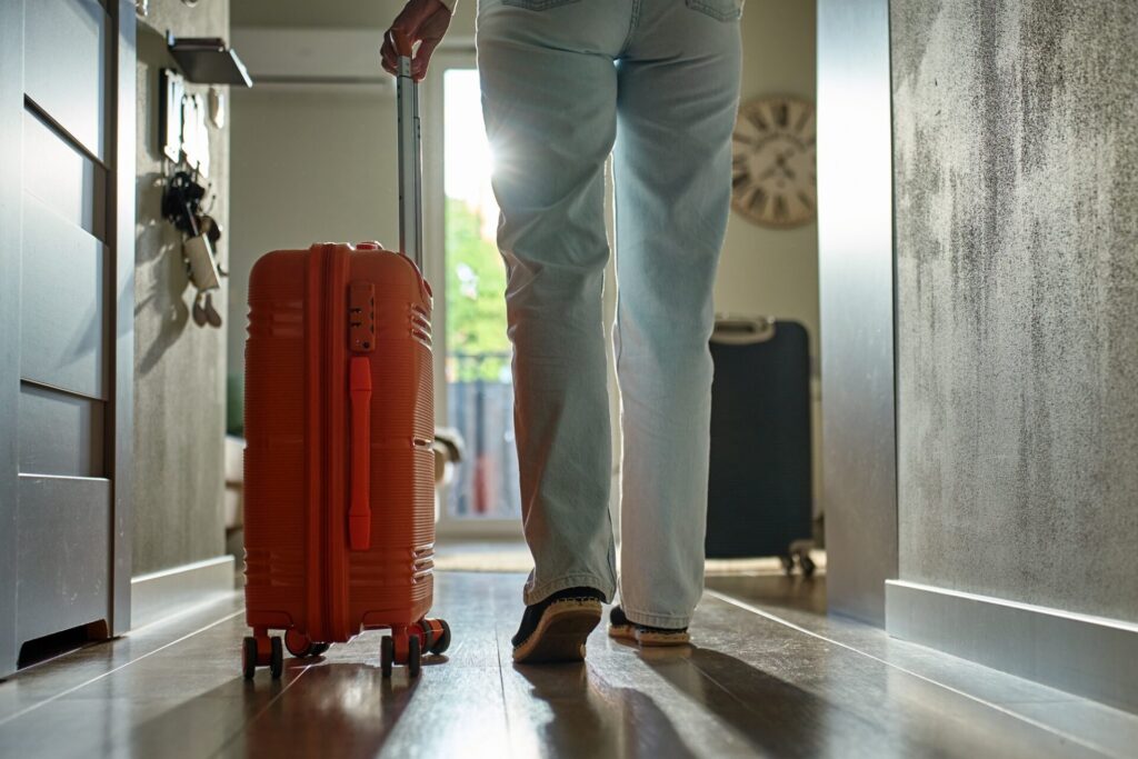 Woman rolls suitcase down hallway in apartment. Departure moment