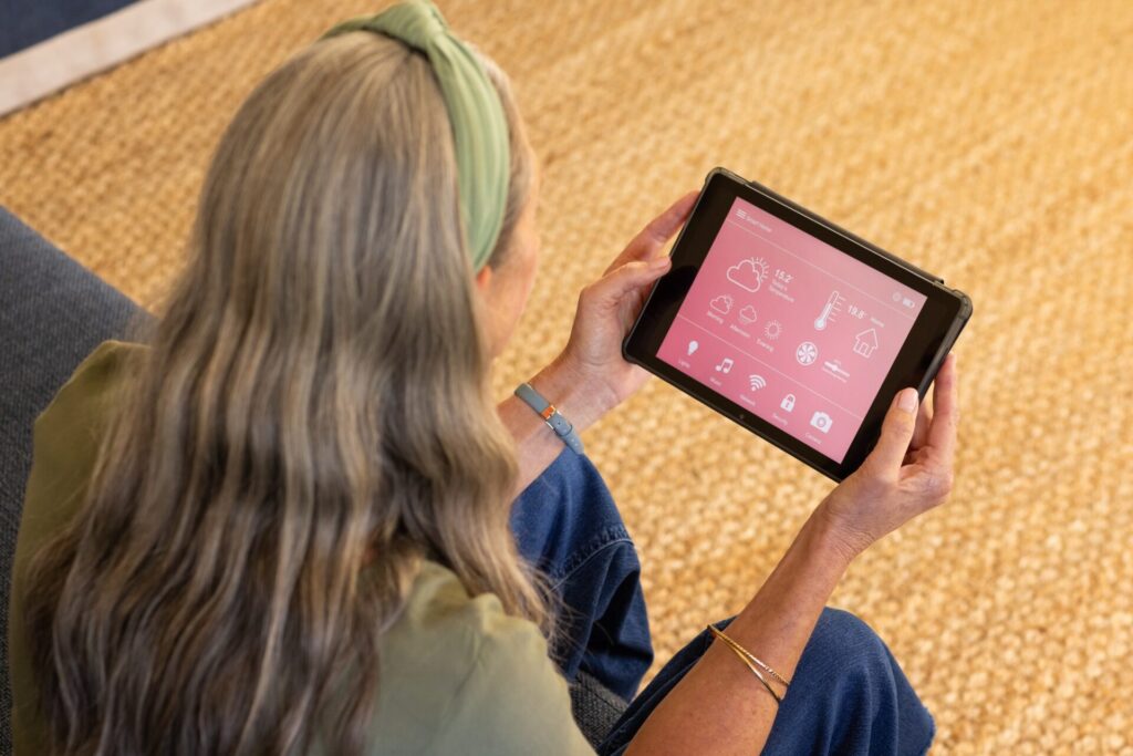 Using tablet, mature woman controlling smart home devices in living room